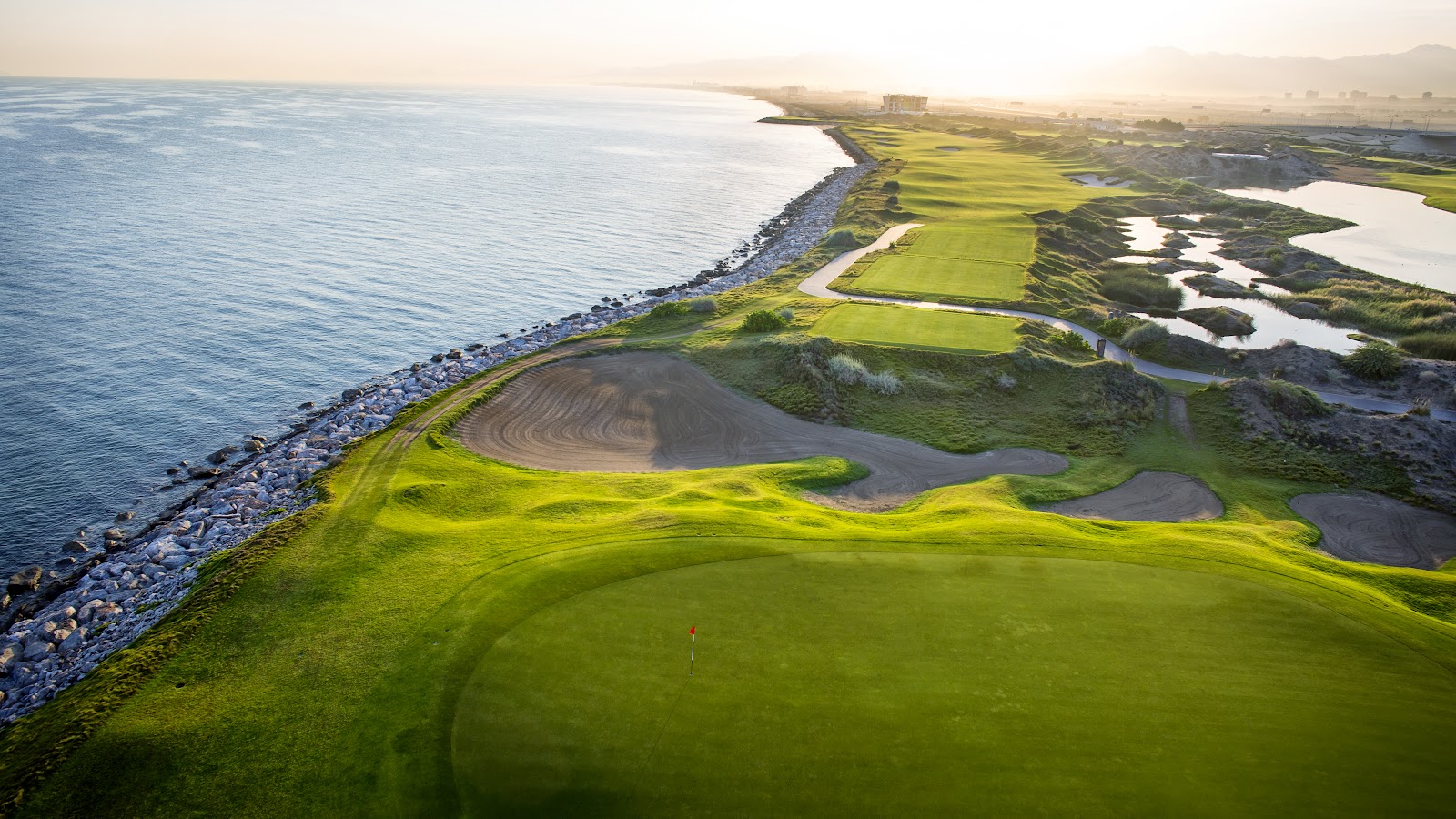 Links style fairways and bunkering at Al Mouj Golf in Muscat, with the Gulf of Oman beyond the dune grasses