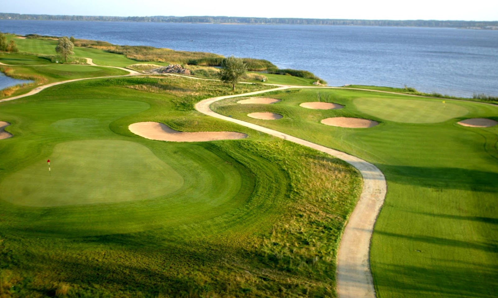 Fairway and water hazard at Ozo Golf Club inside Riga, Latvia, with pines lining the hole on a clear summer day