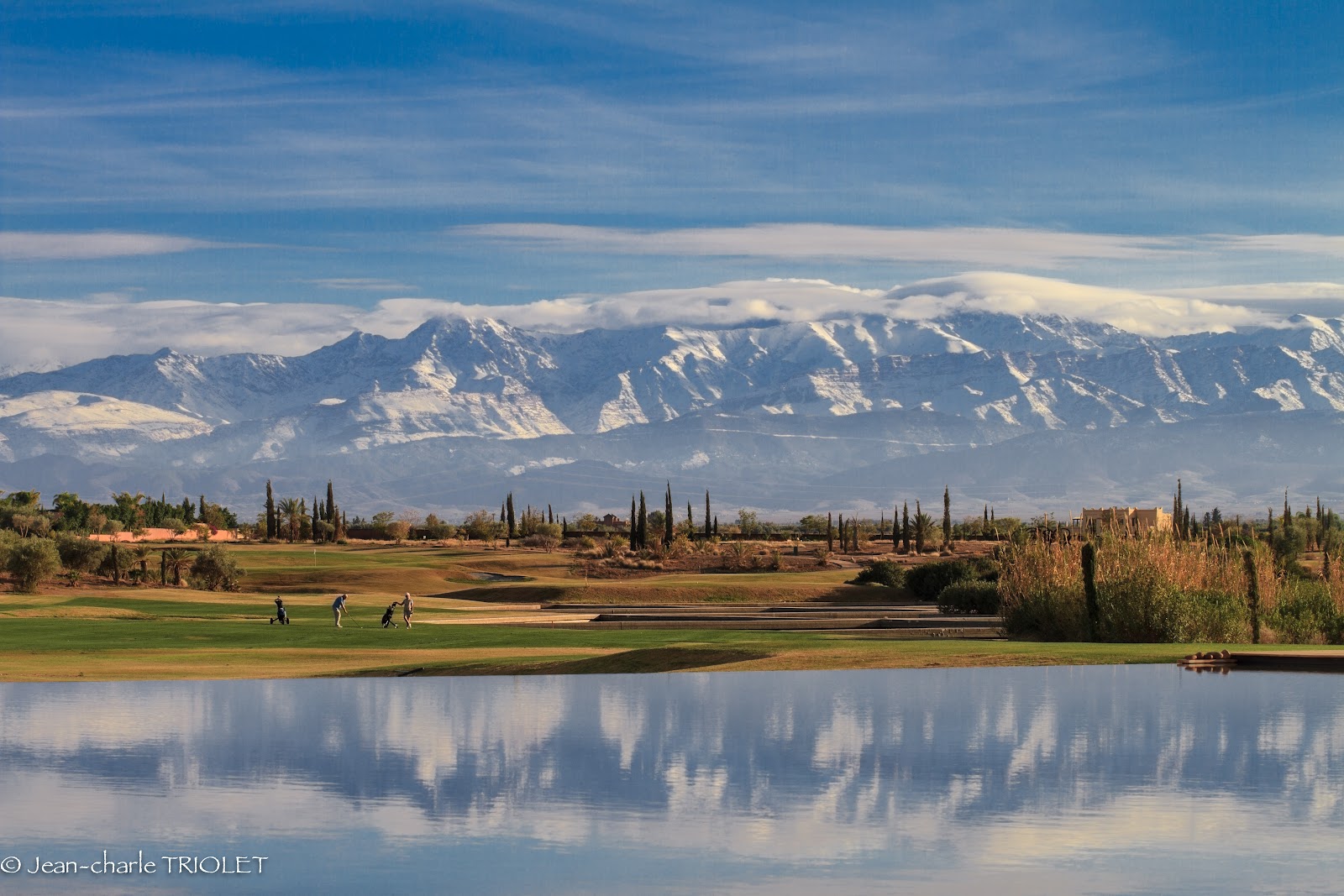 Al Maaden Golf Resort, broad fairways framed by water features and palms with the snow capped Atlas Mountains beyond at Marrakech, Morocco